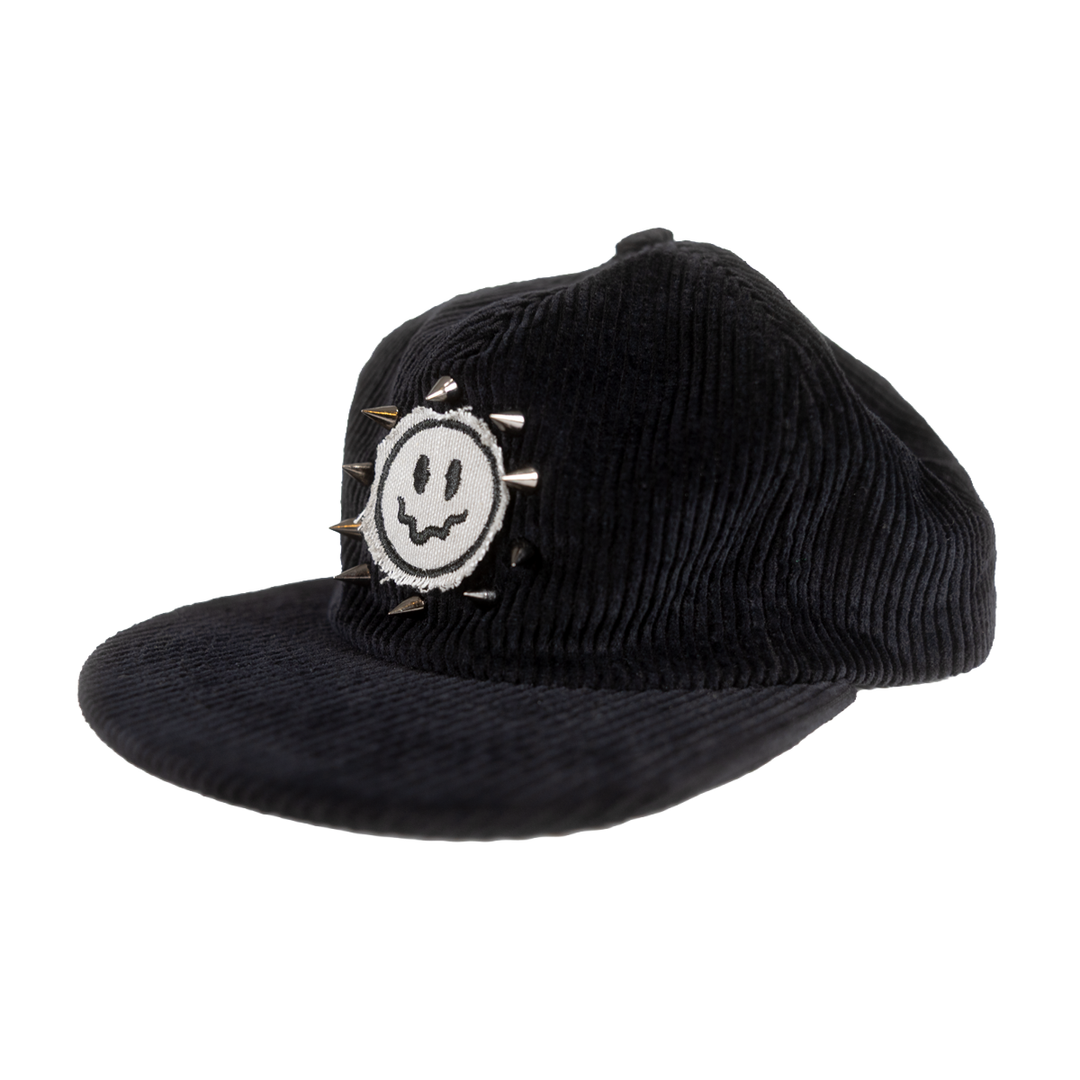 Angled view of black corduroy hat with a spiked smiley patch